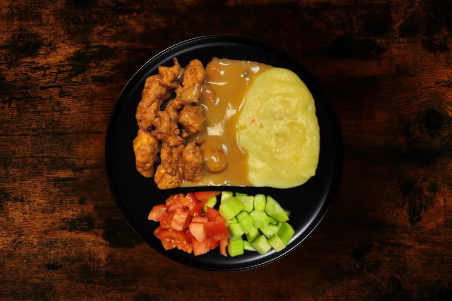 Chicken bites with pepper sauce and mashed potatoes with side dish tomatoes cucumbers